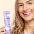 Woman holding a purple skincare product with a beige background