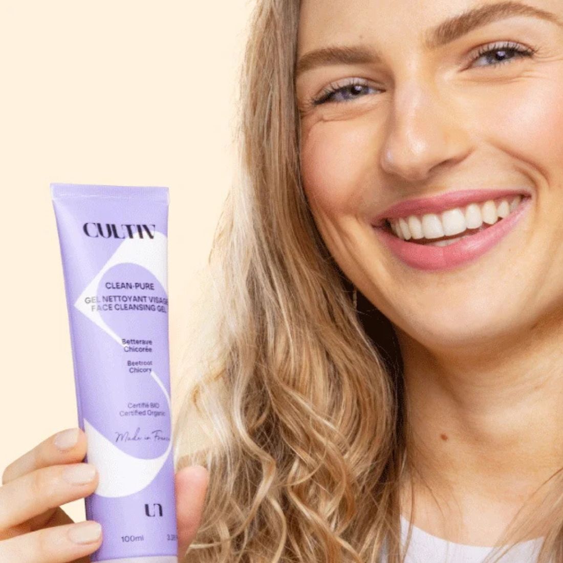 Woman holding a purple skincare product with a beige background