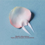 A dollop of pale pink and white cream on a textured light blue background, with a rose petal shape behind it and small Finnish text near the bottom.