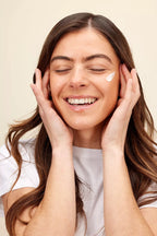 Woman applying cream to her face with a beige background