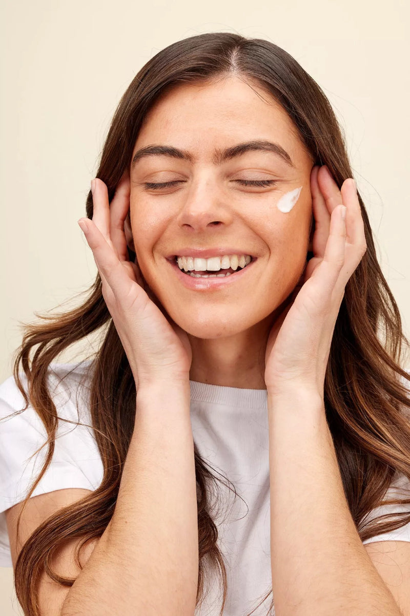 Woman applying cream to her face with a beige background