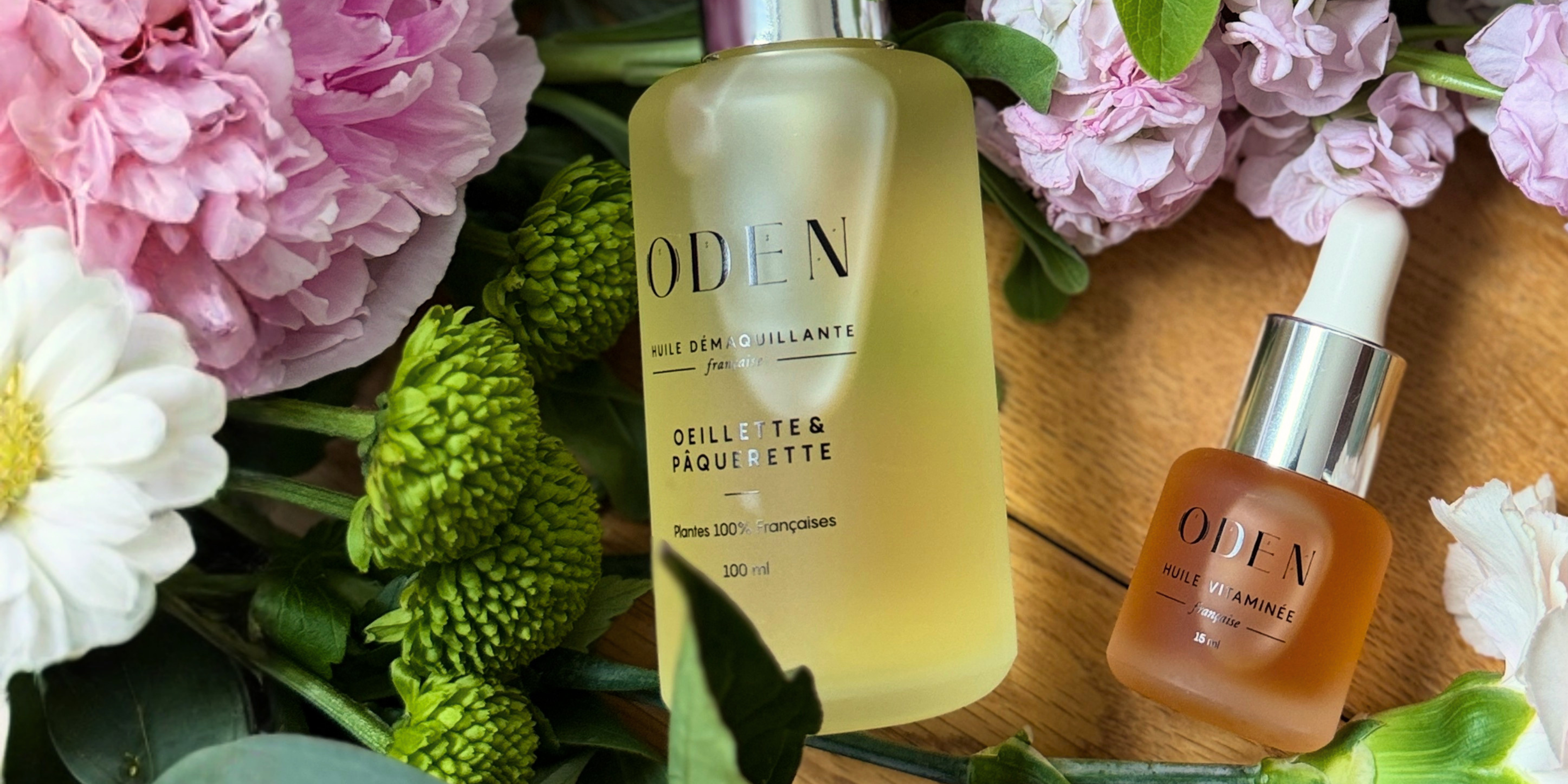 Two ODEN skincare products surrounded by flowers on a wooden surface