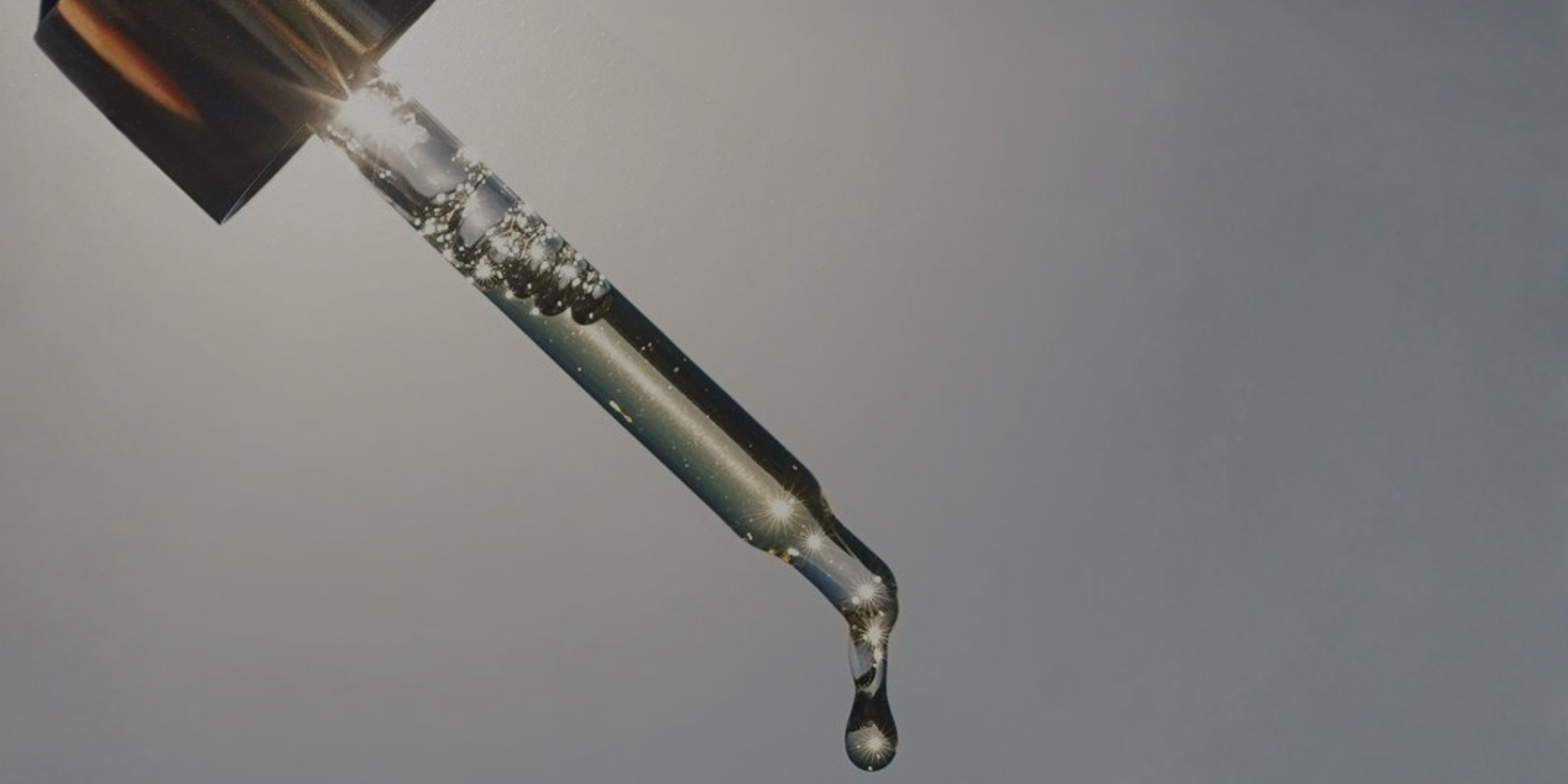 Close-up of a dropper with liquid dripping against a gray background